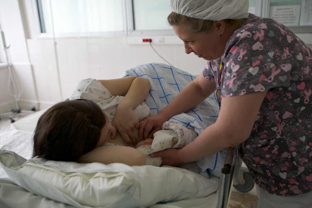 Акушерка прикладывает новорождённого к груди матери
