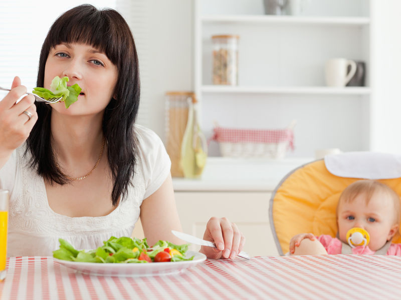 Молодая мама ест салат из свежей зелени