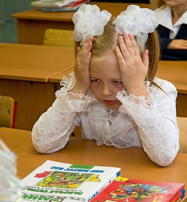 Недовольная девочка хватается за голову, сидя за партой
