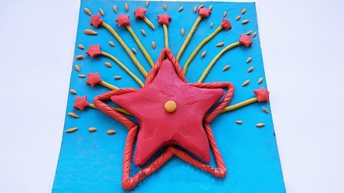 Звезда в центре открытки, её обрамляет красный жгутик, а сверху располагается шлейф салюта