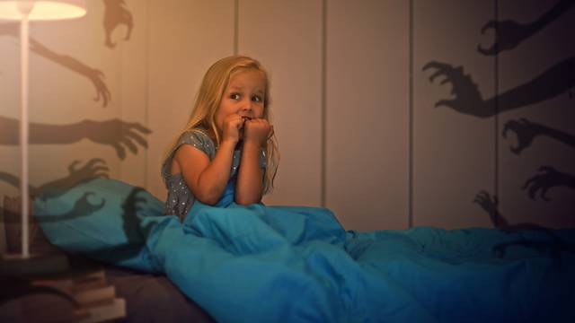 Испуганная девочка сидит на кровати, рядом тени рук