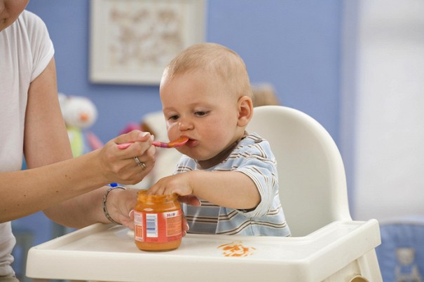 Женщина кормит младенца пюре из баночки
