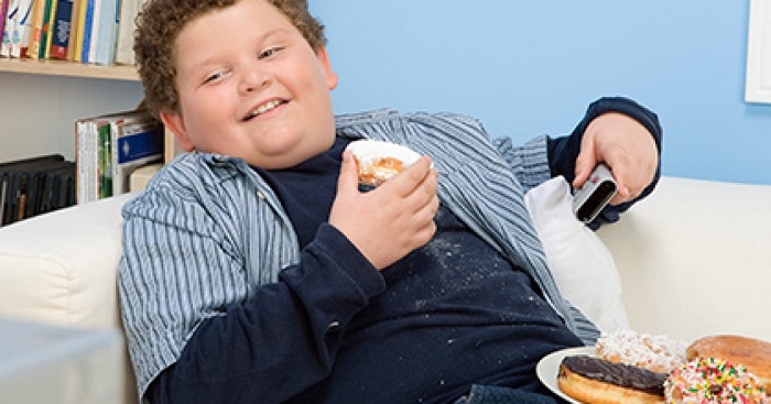 Мальчик с избыточным весом держит в руках пирожное