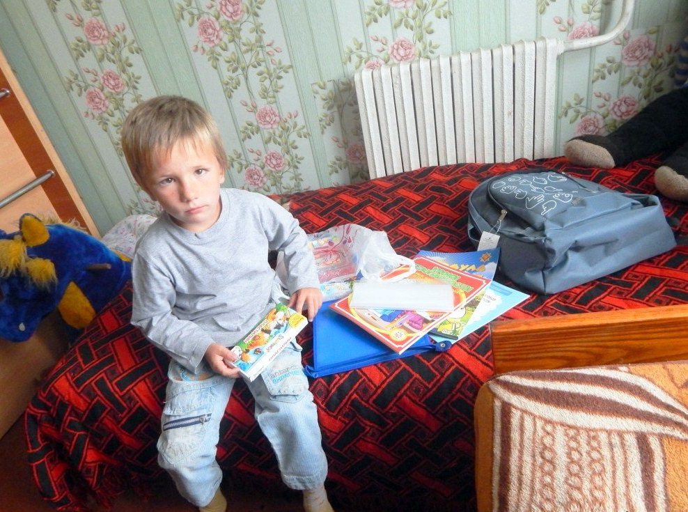 Мальчик сидит на кровати, рядом — книжки и канцтовары