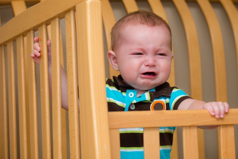 Младенец стоит в своей кроватке и плачет