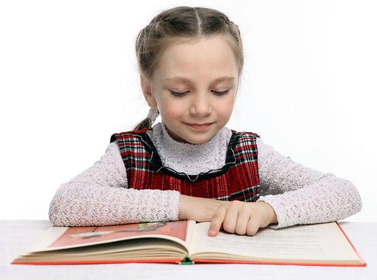 Девочка сосредоточенно читает книгу, проводя пальцем по тексту