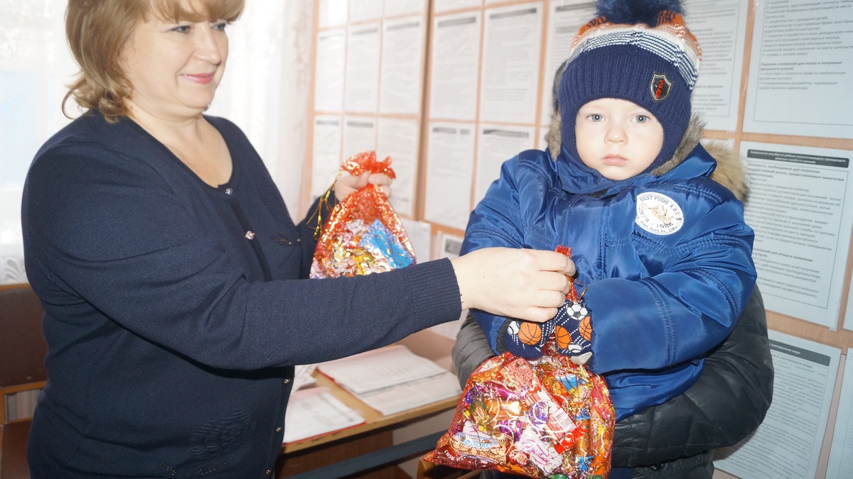 Сотрудница Фонда социальной защиты вручает ребёнку новогодний подарок