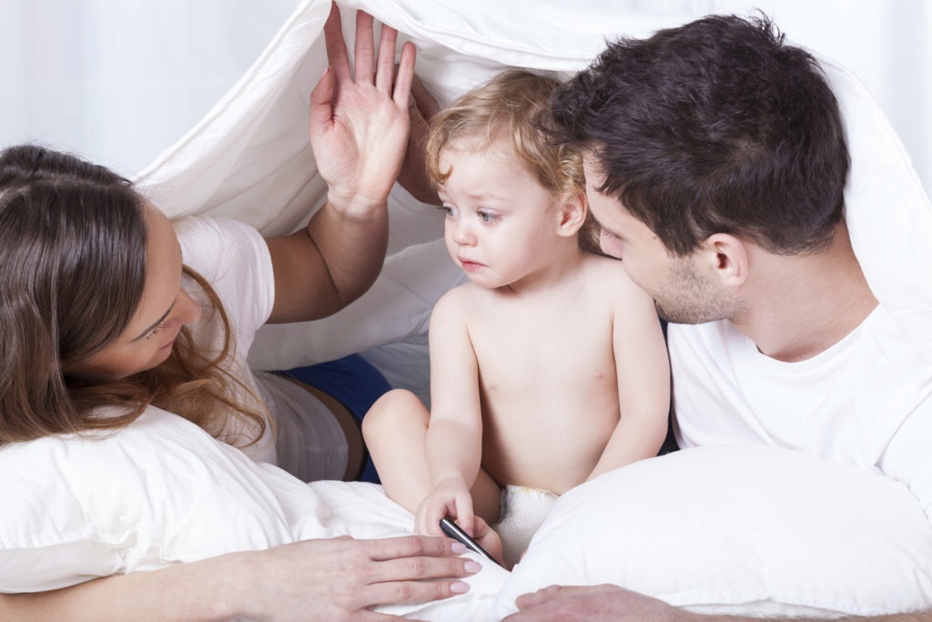 Ребёнок примерно 1,5 лет под одеялом в постели с родителями