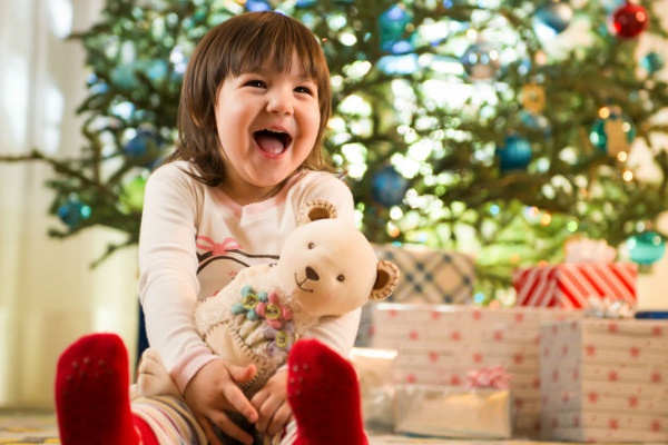 Девочка держит в руках нового плюшевого мишку и радостно смеётся