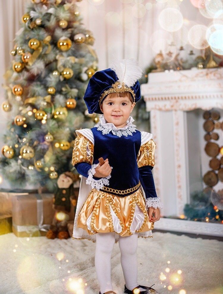 Двухлетний мальчик в костюме принца на фоне новогодней ёлочки