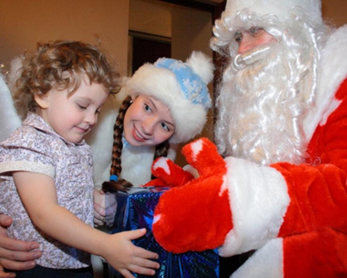 Дед Мороз со Снегурочкой вручают маленькой девочке подарок