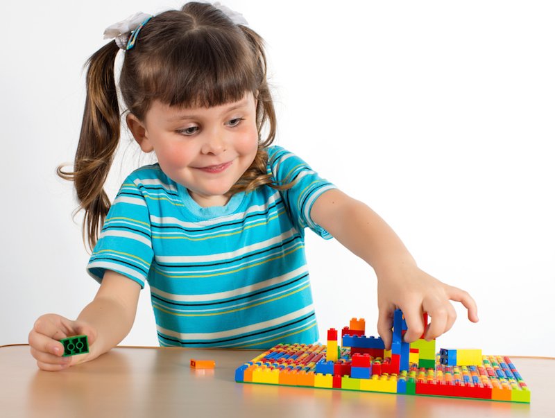 девочка собирает детали из конструктора Лего