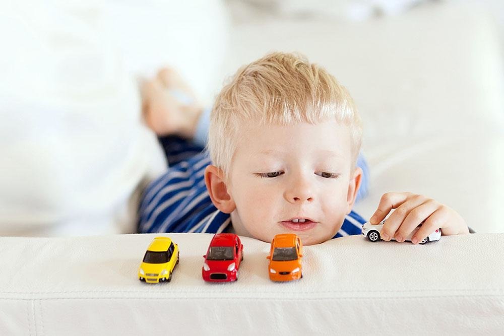 мальчик лёжа играет с машинками