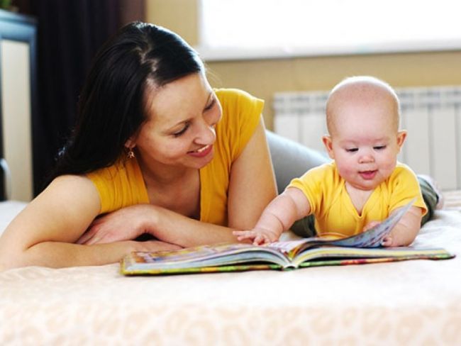 ребёнок лёжа листает книжку, мама улыбается рядом
