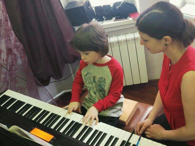 ребёнок играет на фортепиано, рядом сидит учительница