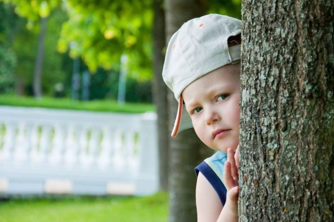 Мальчик прячется за деревом и испуганно выглядывает оттуда