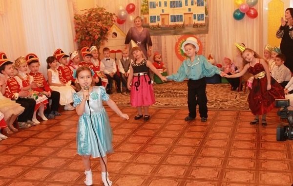 Девочка-дошкольница одна поёт песню в микрофон на утреннике в детском саду