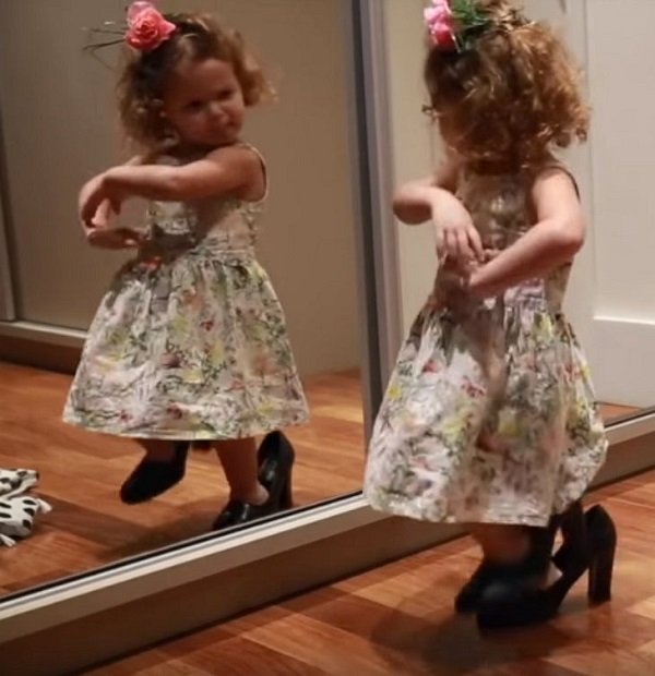 Маленькая девочка танцует перед зеркалом в маминых туфлях