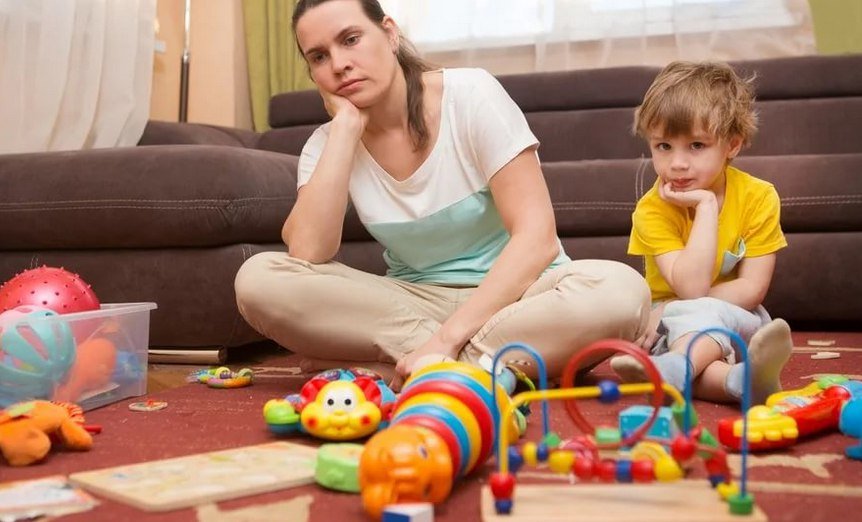 Мама сидит с сыном среди разбросанных игрушек