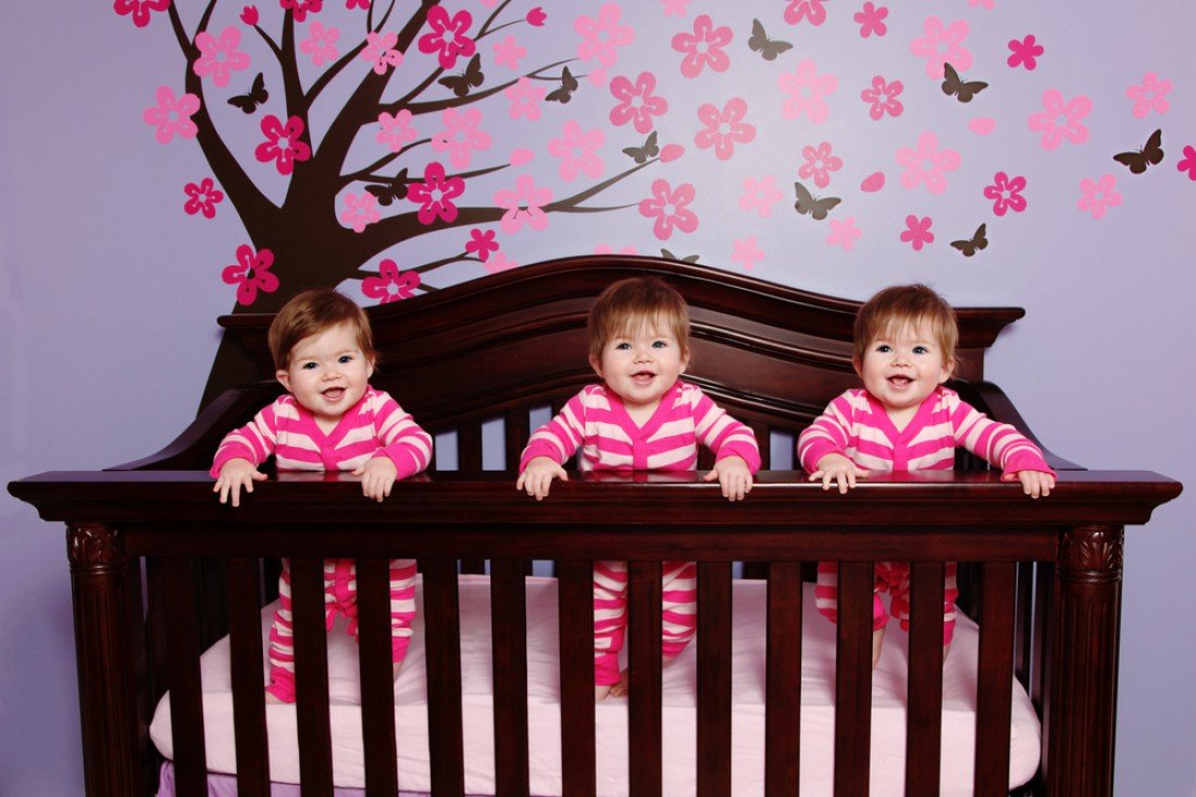 Младенцы-тройняшки стоят в кровати