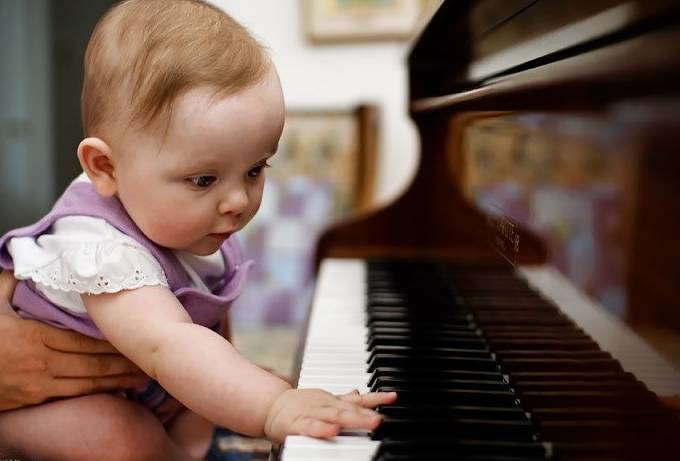 Грудной малыш нажимает пальчиками на клавиши фортепиано