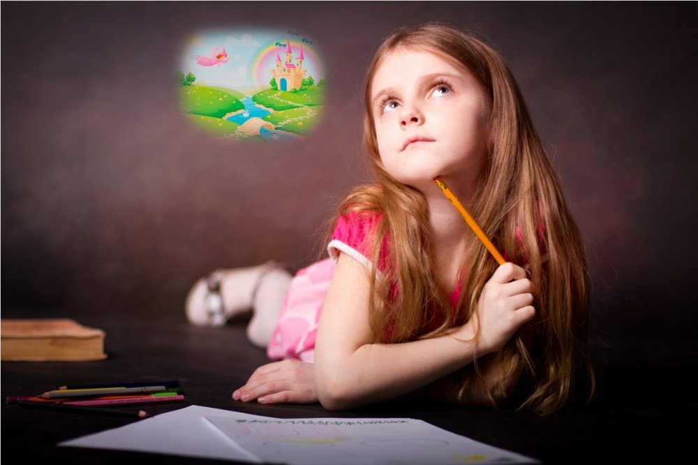 Девочка лежит на кровати с рисунком и карандашами и воображет сказочный мир