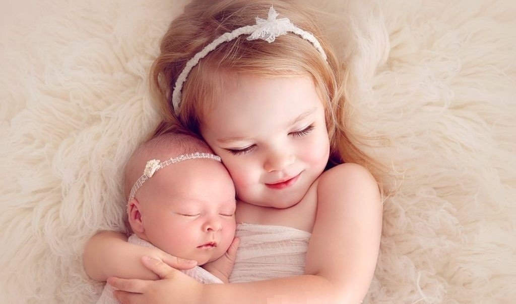Маленькая девочка обнимает свою новорождённую сестричку