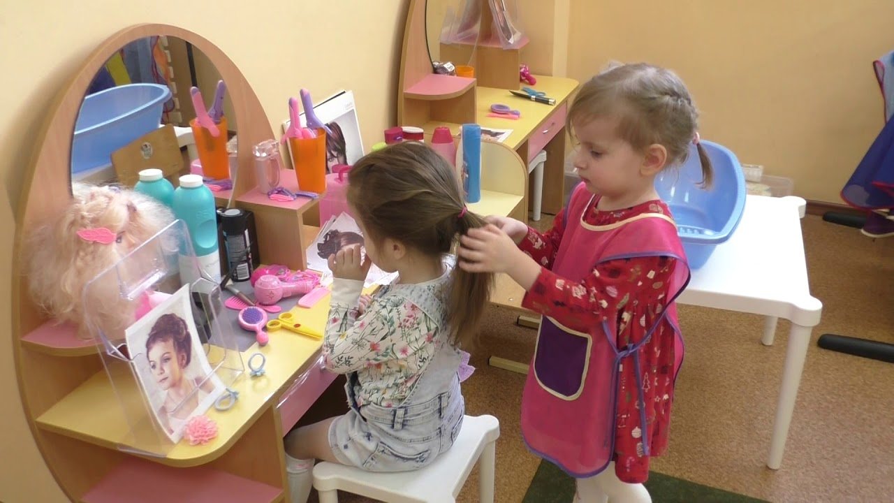 Одна девочка сидит перед зеркалом, а вторая делает ей причёску