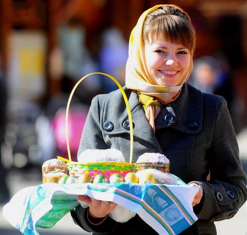 Улыбающаяся девушка держит поднос с куличом и яйцами