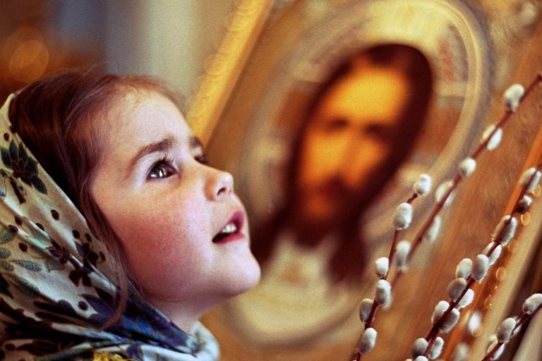 Девочка в храме с удивлением смотрит вверх, держа веточку вербы