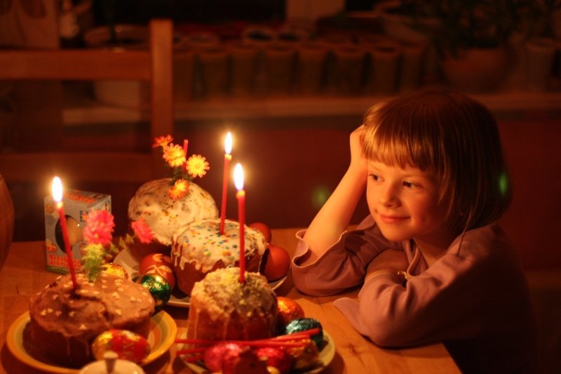 Девочка сидит за столом и любуется на пасхальные куличи