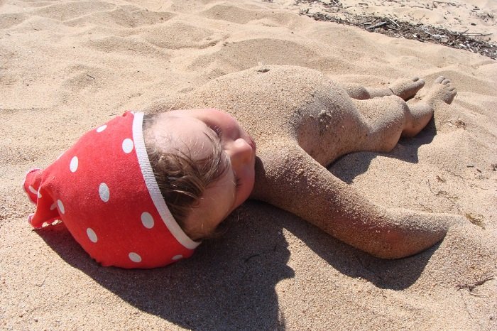 Маленькая девочка лежит на песке, вся покрытая песком