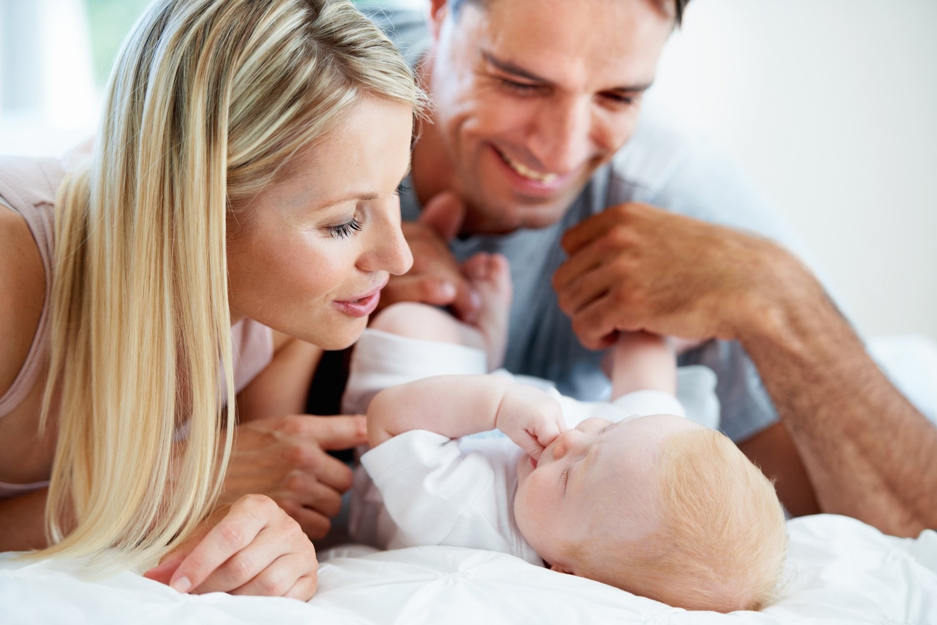 Папа держит за руки младенца, рядом мама