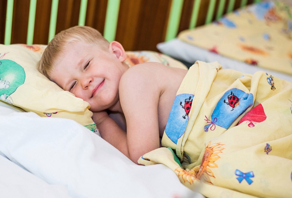 Мальчик лежит на кровати, зажмурив глаза